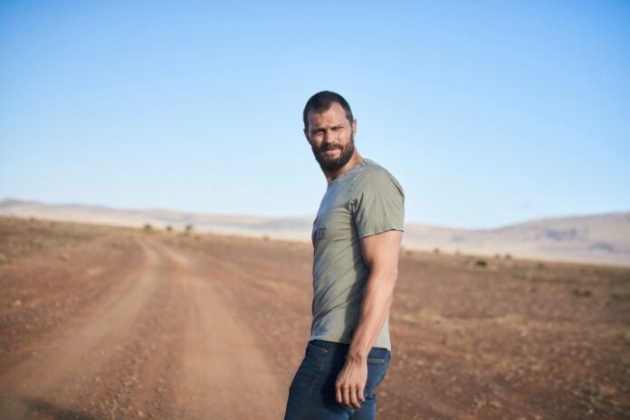 Jamie Dornan guida un'auto e guarda nello specchietto retrovisore un camion che si avvicina a lui in una scena di The Tourist.