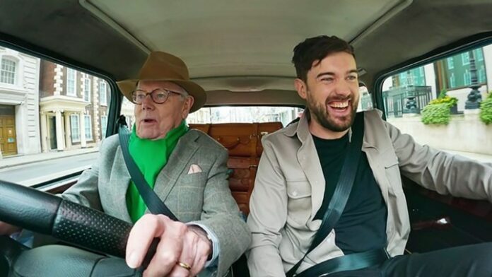Jake Whitehall in macchina con suo padre Michael alla guida, suo padre che sembra terrorizzato e Jack che sorride in una scena di Jack Whitehall: Travels with My Father su Netflix.