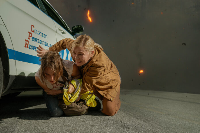 Cailee Spaeny e Kirsten Dunst sono accovacciate accanto a un'auto in Civil War.