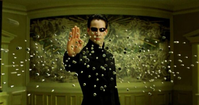 Keanu Reeves ferma una pioggia di proiettili con la mente in un'immagine di Matrix