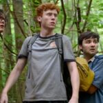 I tre membri di Please Don't Destroy in piedi in una foresta con aria spaventata in una scena di Please Don't Destroy: The Treasure of Foggy Mountain.